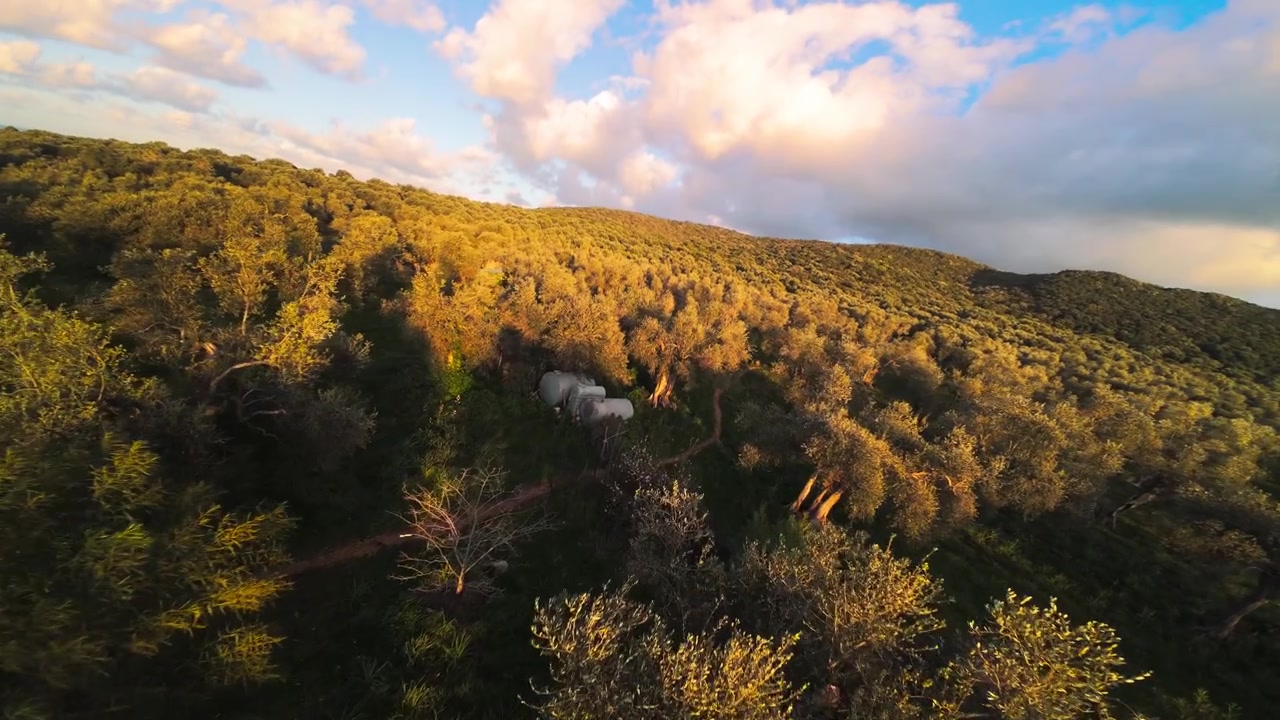 Volo cinematografico di drone aereo su una fattoria agrituristica ed ecoturistica sostenibile ed ecologica con yurte e ulivi durante un tramonto vibrante. Ecovillaggio e vita sostenibile nella natura