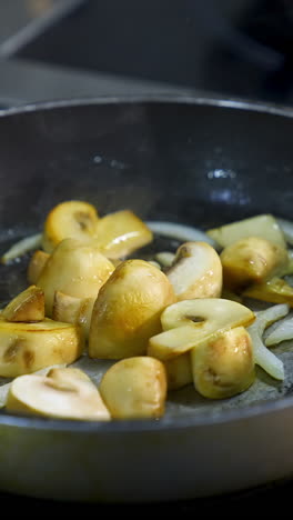 cooking mushrooms in frying pan. delicious mushrooms are frying with onions in oil on a stove. close-up. vertical video