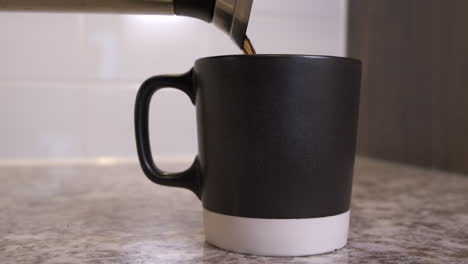 Freshly-brewed-filter-coffee-being-poured-from-metal-carafe-into-brown-and-white-mug