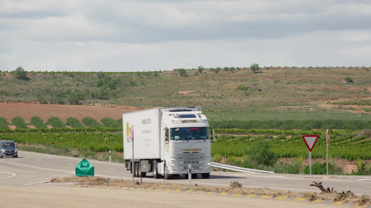 Vehicles Driving on a Rural Road Past Vineyards and Hills