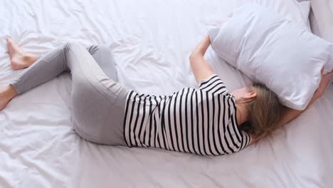 a woman covers her head with a pillow because of pain while lying on the bed lonely upset woman covered head with pillow while lying on bed in bedroom in grief and sadness