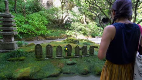 a woman walks through a kamakura temple in japan, and says a prayer in front of small statues of buddhas