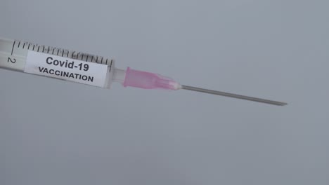 syringe with covid 19 vaccine fluid drops on needle flick by finger, close up shot