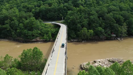 following aerial view of dark van on bridge crossing river and railway in countryside of west virginia, usa, cinematic drone shot