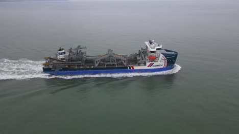 4k 30fps aerial drone flight around a merchant ship out at sea showing waves flowing behind and the needles white cliffs on the coast of the isle of wight in the background