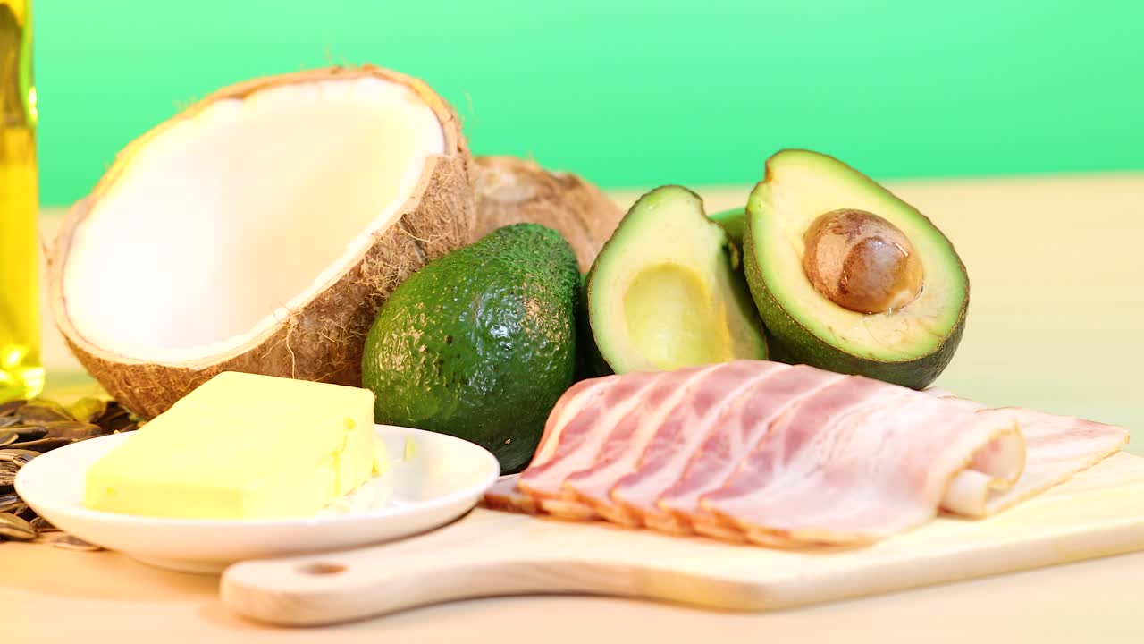 A vibrant display of various healthy fats including oils, nuts, and avocados on a wooden surface with bright lighting