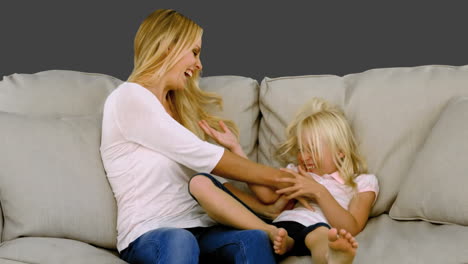 mother tickling her daughter on sofa