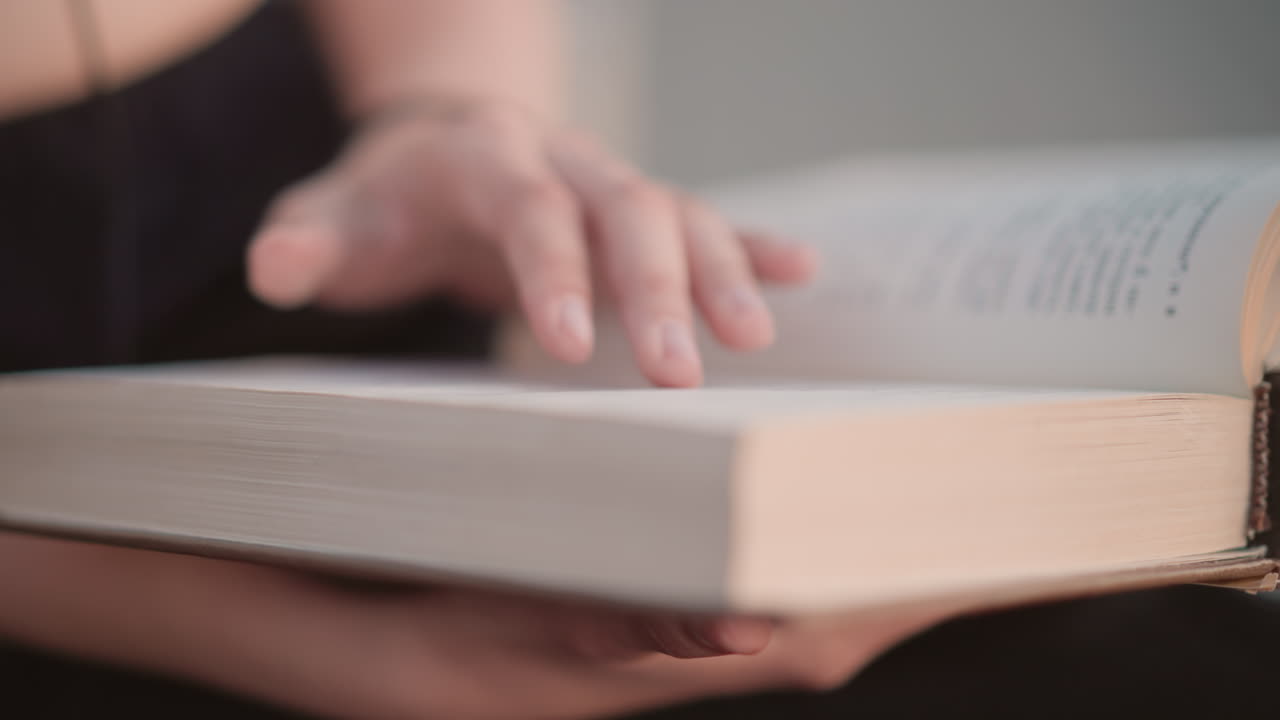 Koncentreret læsning: Kvinde studerer omhyggeligt en gammel bog. Indendørs scene med en kvinde, der undersøger ældgamle sider opmærksomt. Kaukasisk kvinde fordybet i at læse en ældre paperback under et blidt lys.