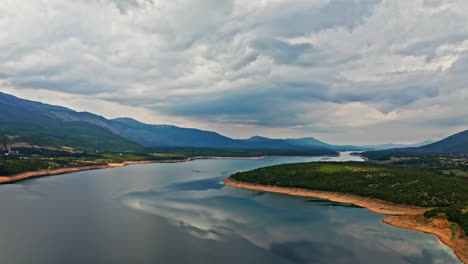 Cámara-Aérea-Volando-Lateralmente-En-Una-Amplia-Toma-De-Un-Hermoso-Paisaje-Montañoso-En-Un-Día-Nublado,-Con-Bonitos-Reflejos-En-Un-Lago