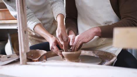 Close-Up-Of-Female-Teacher-Helping-Man-Sitting-At-Wheel-In-Pottery-Class