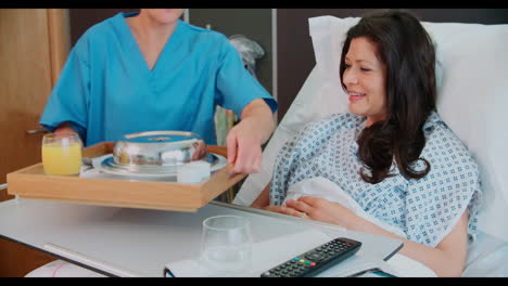 paciente femenina en una cama de hospital siendo servida una comida por ordenado