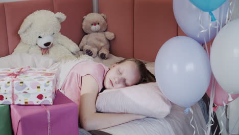 un niño duerme en su cama, al lado de cajas de regalos y globos.