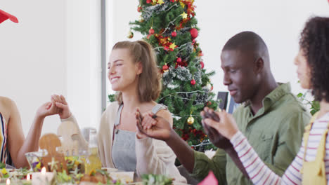 Happy-group-of-diverse-friends-sitting-at-table-and-eating-dinner,-praying-together