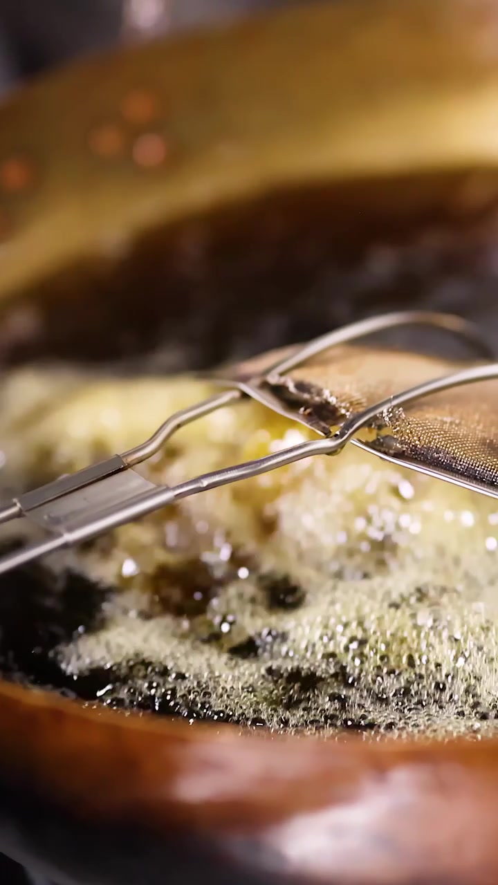 Close-up shot of food frying in hot oil within a traditional brass cooking vessel.