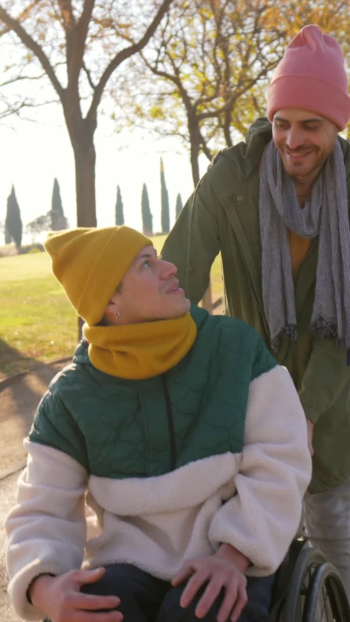 Man pushing a friend in a wheelchair through a park