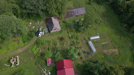 the drone circles to the right, capturing a vibrant farm with people enjoying their time outdoors. a child runs around the garden, adding life to the farm setting.