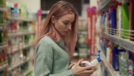 blonde woman reads label of household products in supermarket