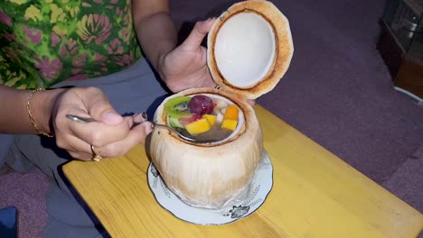 Tasty-fruit-salad-made-inside-coconut,-tasted-by-woman,-close-up