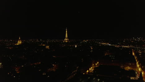 Vista-Aérea-De-La-Metrópolis-Nocturna,-Hacia-Adelante-Vuela-Hacia-La-Torre-Eiffel-Iluminada.-Famosa-Estructura-Alta.-París,-Francia