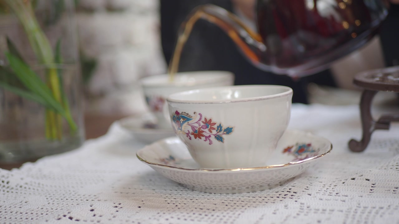 Pouring Hot Tea into an Ornate Vintage Teacup on a Lace Tablecloth