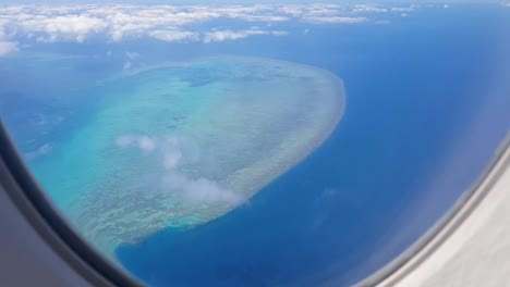 Flying-over-the-Great-Barrier-Reef-and-stunning-blue-ocean-in-an-airplane,-east-coastline-of-Australia