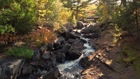 Hochfliegender-Schuss-über-Einen-Waldbach,-Der-über-Den-Felsigen-Waldboden-Läuft-Und-Die-Bunten-Herbstfarben-Der-Vegetation-Zeigt