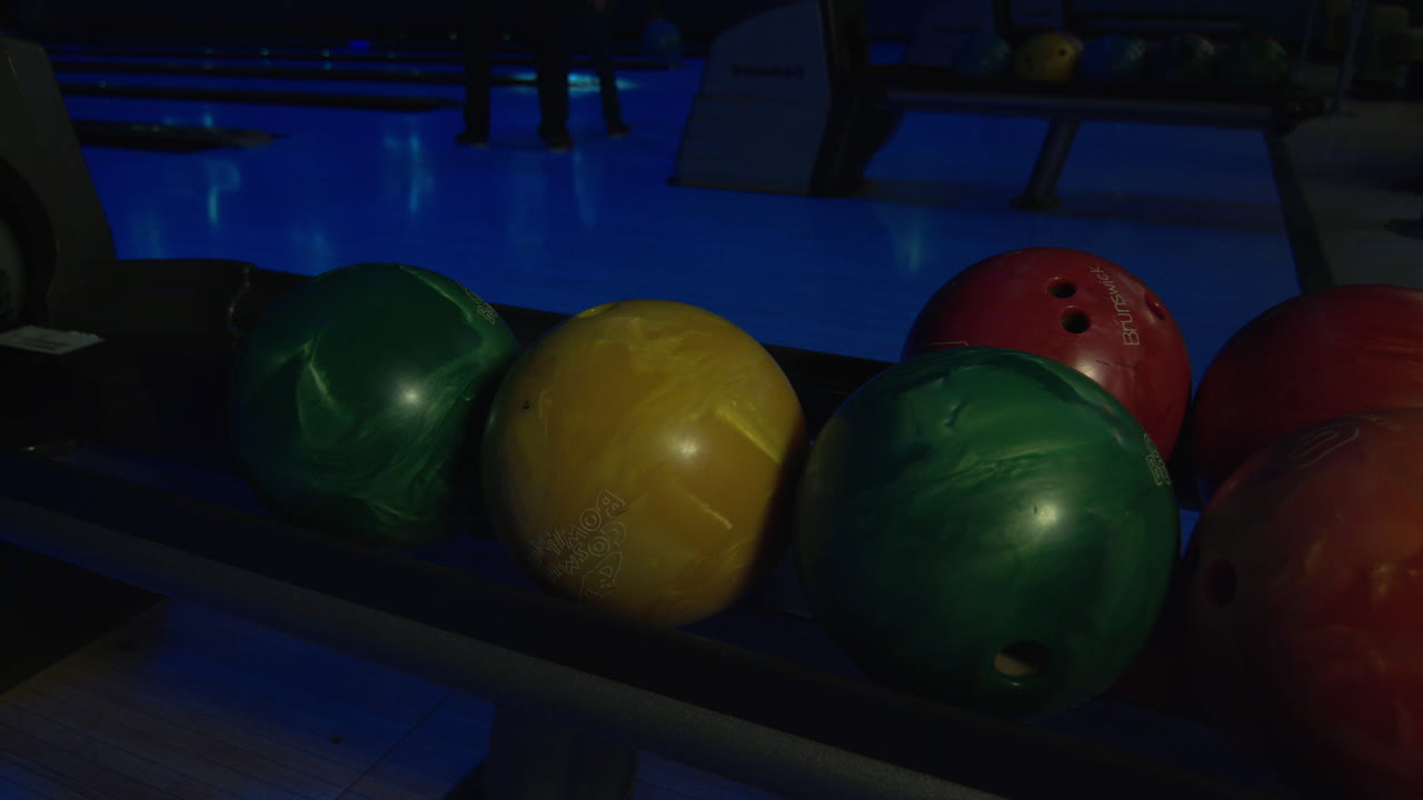 A hand picking up a green bowling ball  from the ball return in night bowling