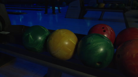 a hand picking up a green bowling ball  from the ball return in night bowling