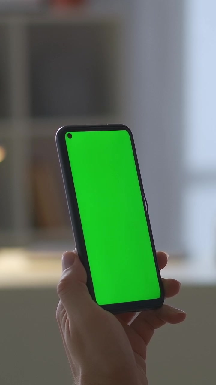 Primo piano di una mano che tiene uno smartphone in verticale con schermo verde