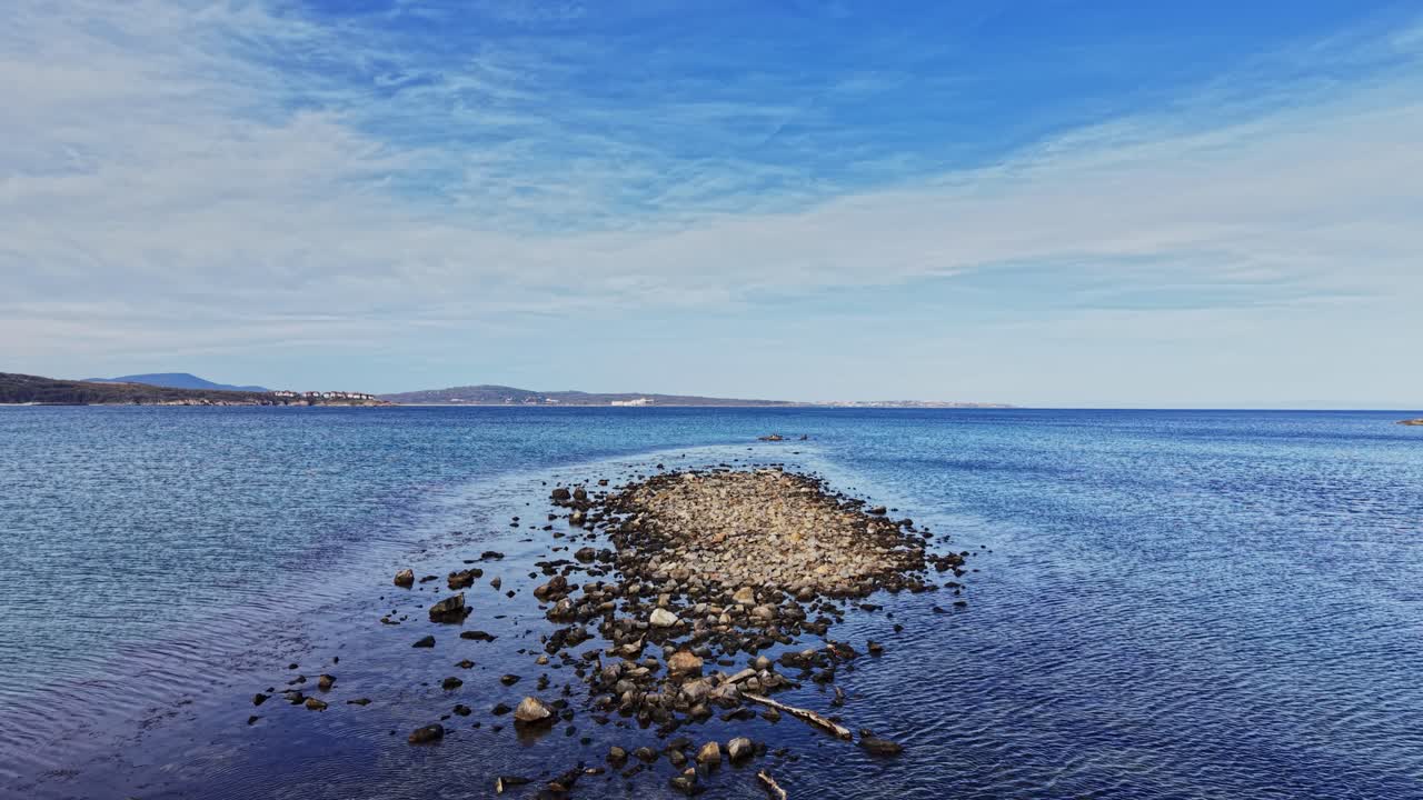 Aerial view of rocky shore and clear blue waters under bright sky