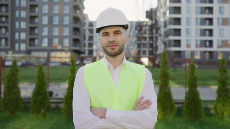 portrait of a male engineer or construction worker in a hard hat and safety vest at a building site