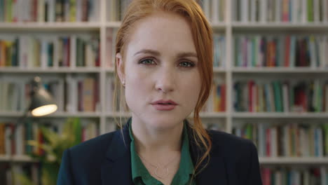 portrait of attractive young red head business woman intern turns head looking pensive serious at camera in library study background