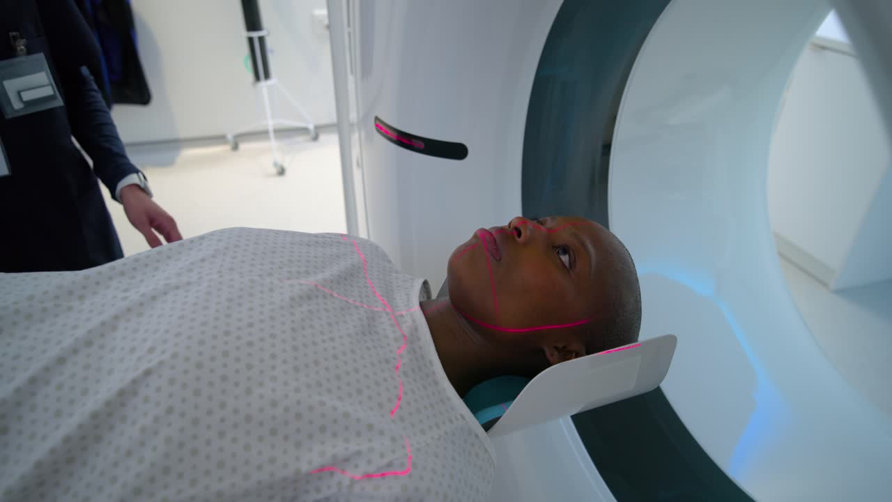 Tecnico TAC con hijab che modifica il pannello dopo i laser rossi mentre una donna afroamericana è sdraiata per la scansione