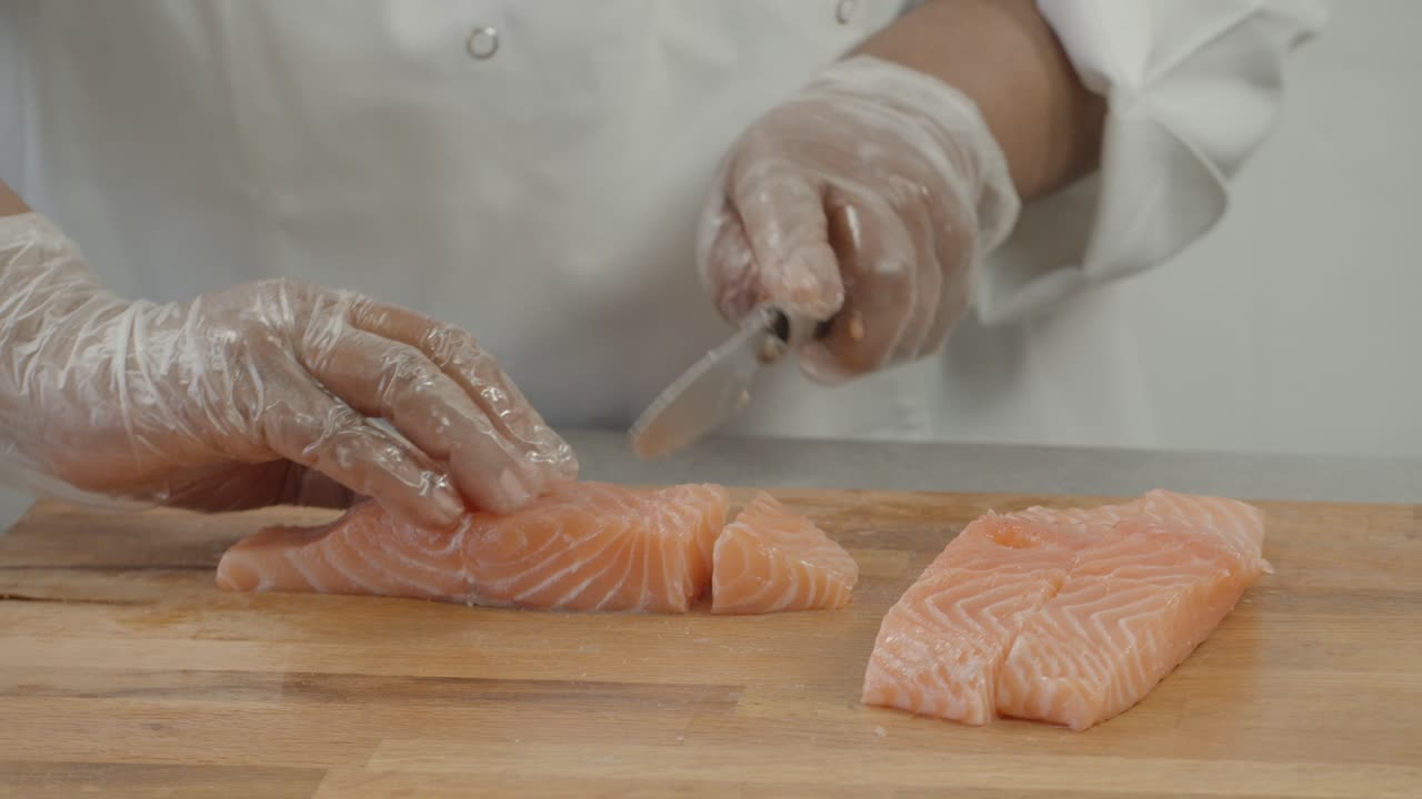 Close up of Professional male chef hand using fish fillet knife slice fresh orange salmon meat on cutting board in restaurant kitchen