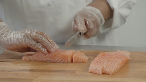 Close-up-of-Professional-male-chef-hand-using-fish-fillet-knife-slice-fresh-orange-salmon-meat-on-cutting-board-in-restaurant-kitchen