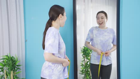 slim asian young woman measures her waist with a tape measure.