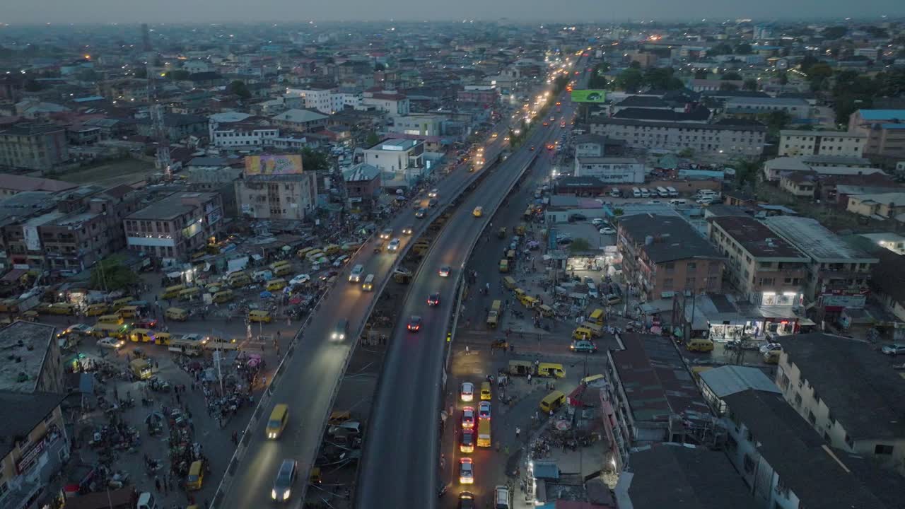Affascinante ripresa aerea: le luci serali danzano mentre i veicoli scivolano sul ponte di Lagos, una sinfonia urbana ipnotizzante catturata in movimento.