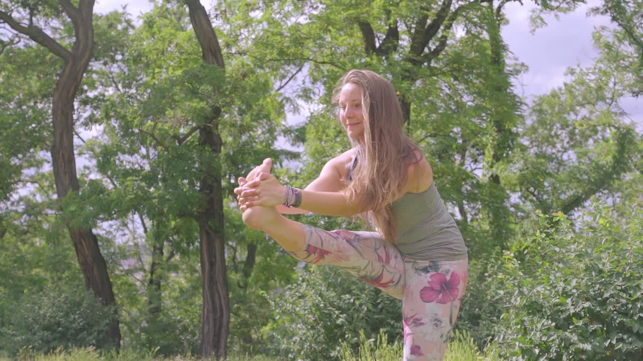 mujer caucásica tiene pose de yoga al aire libre en la naturaleza, tiro a cámara lenta