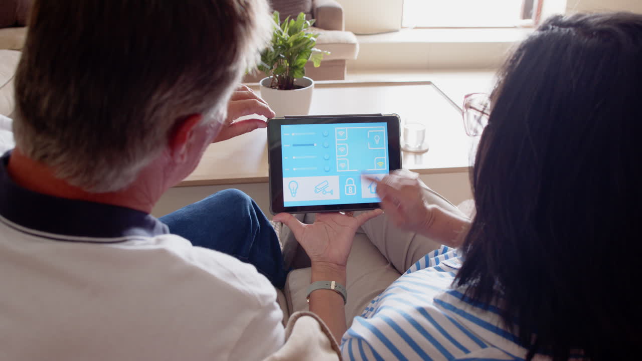 Senior diverse couple using tablet to control smart home devices in living room