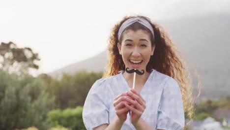 portrait of happy caucasian woman playing with fake moustache