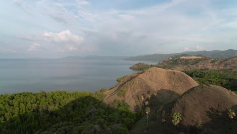 a panoramic view of tropical hills meeting the serene sea under a cloudy sky
