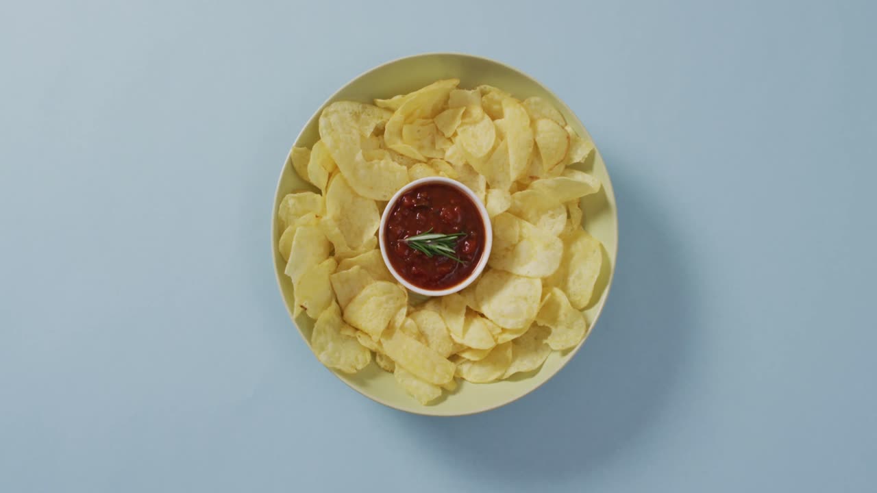 Close up of potato chips in a bowl with sauce on blue surface