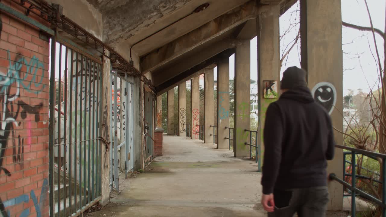 Rear view of man on outer edge walkway of abandoned stadium with graffiti on wall