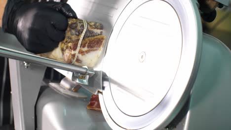 un hombre está cortando un pedazo de carne ahumada con una cortadora automática.