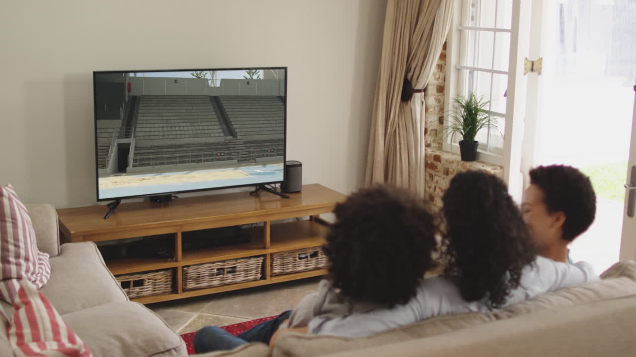 Composizione: famiglia felice seduta a casa insieme che guarda l'atletica del salto in lungo in TV.