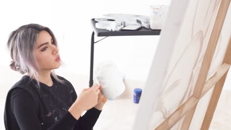 latina artist in a messy look working on painting canvas and check her smartphone