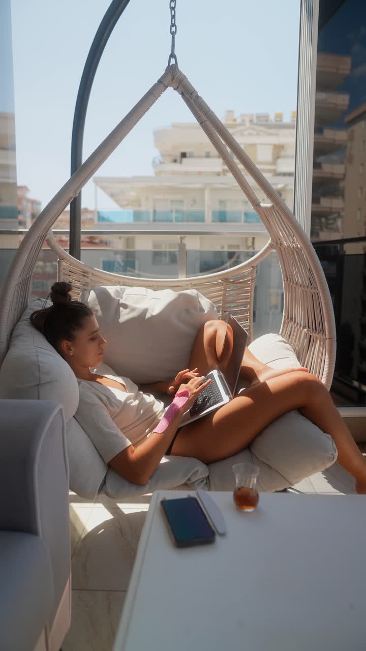 mujer trabajando en una computadora portátil en una silla colgante en un balcón
