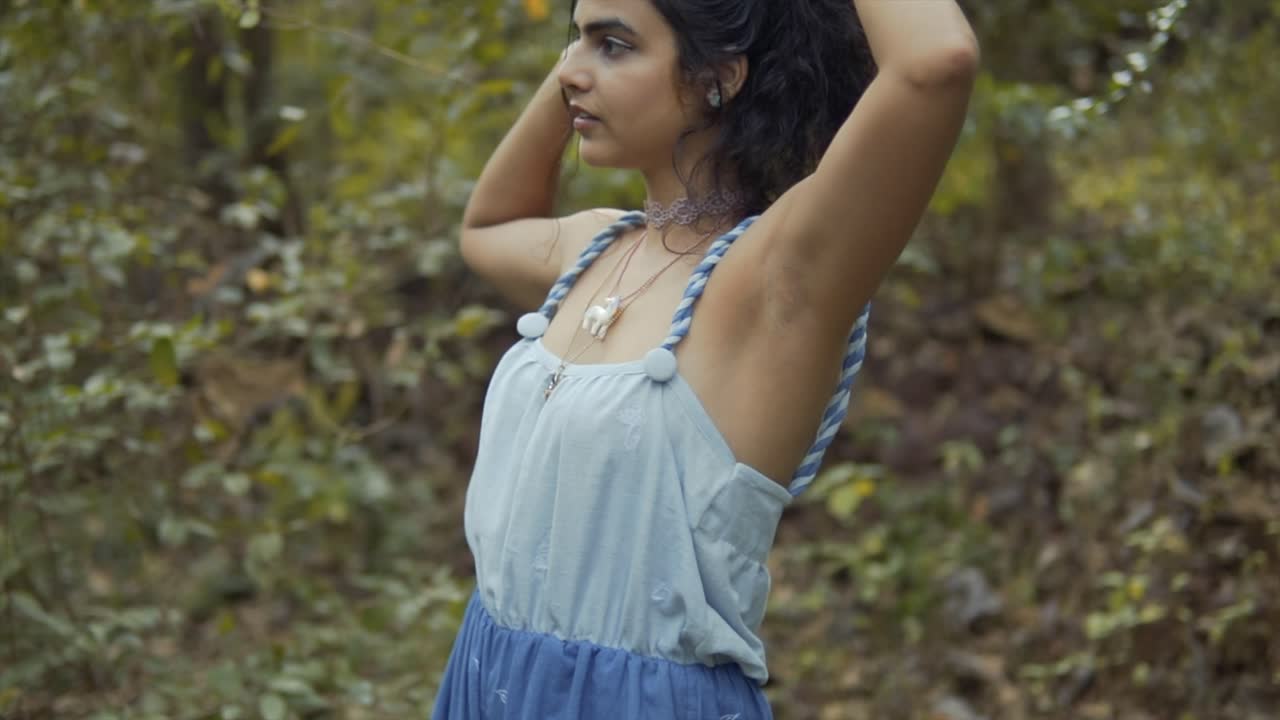 fotografía cinematográfica en cámara lenta de una modelo jugando con su cabello en la selva tropical de goa en la india con un vestido blanco y azul con un collar inspirado en un animal, slomo