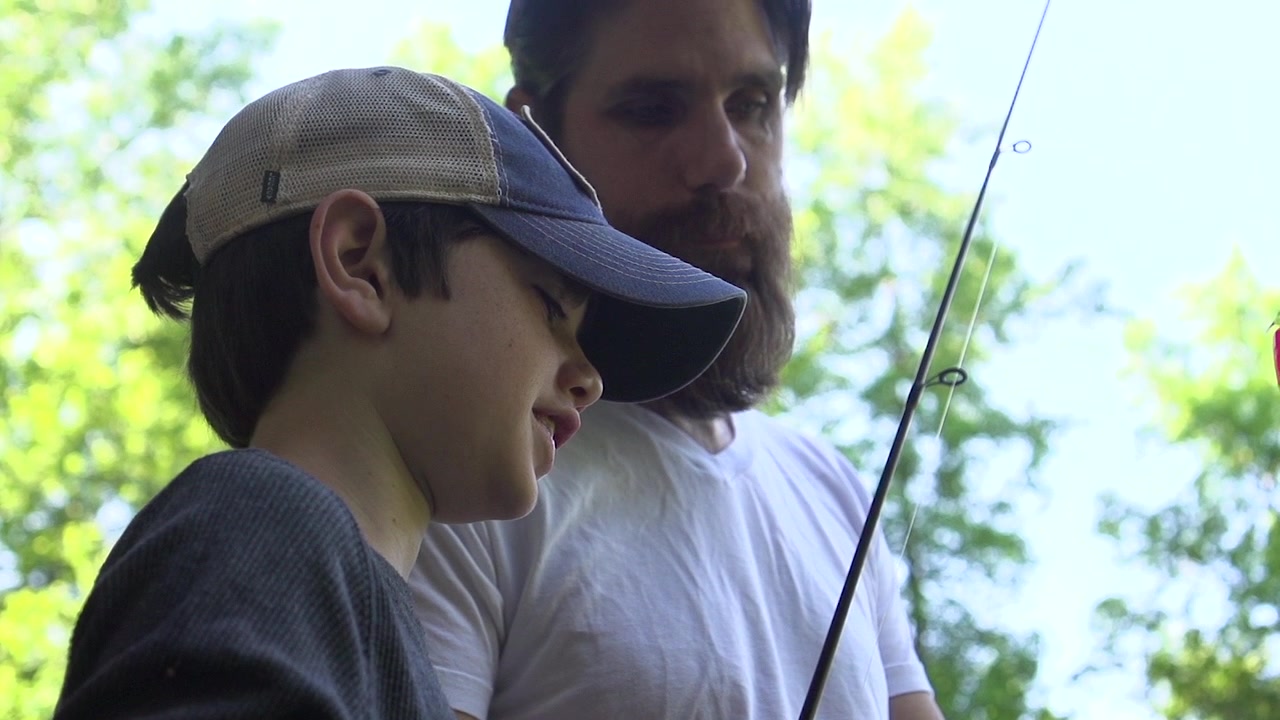 En far og søn fisker ved en dam.