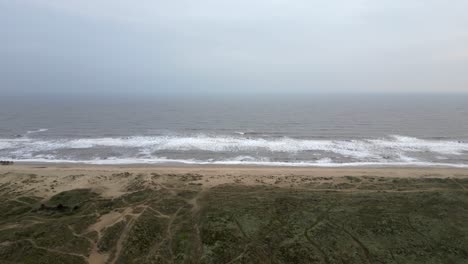 drone flies forward over dunes toward winterton beach and crashing waves